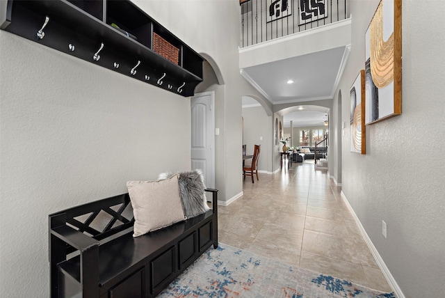 corridor with ornamental molding, a high ceiling, and light tile patterned floors