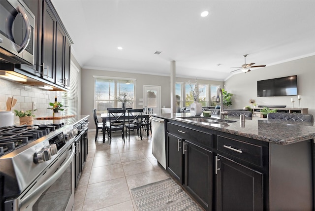 kitchen with tasteful backsplash, stainless steel appliances, ceiling fan, sink, and an island with sink