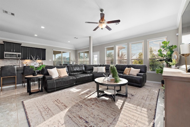 living room featuring ceiling fan, sink, light tile patterned floors, and crown molding