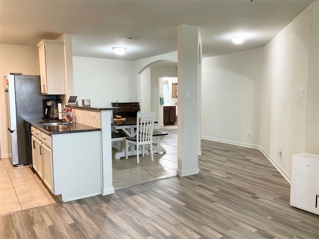 kitchen featuring sink, kitchen peninsula, white cabinets, dark stone counters, and light wood-type flooring