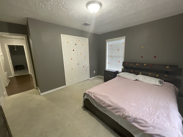 bedroom with light colored carpet, a textured ceiling, and a closet