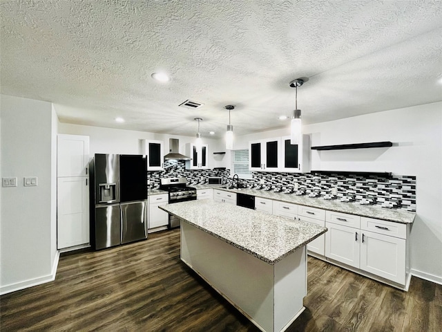 kitchen featuring pendant lighting, wall chimney exhaust hood, a kitchen island, white cabinetry, and stainless steel appliances