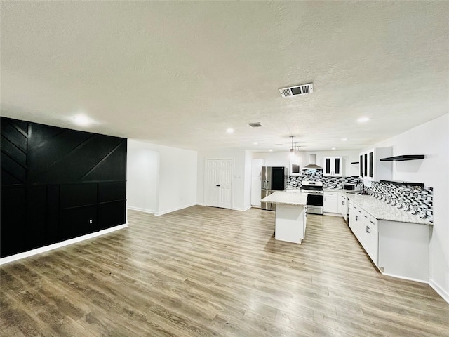 kitchen with appliances with stainless steel finishes, wall chimney exhaust hood, pendant lighting, white cabinets, and a kitchen island