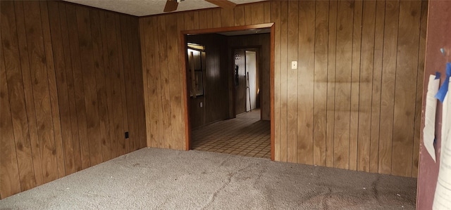 carpeted spare room featuring wood walls and ceiling fan