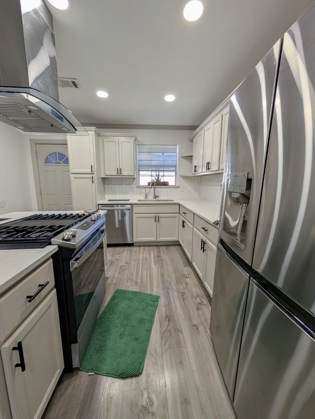 kitchen featuring island exhaust hood, appliances with stainless steel finishes, sink, light hardwood / wood-style flooring, and white cabinets