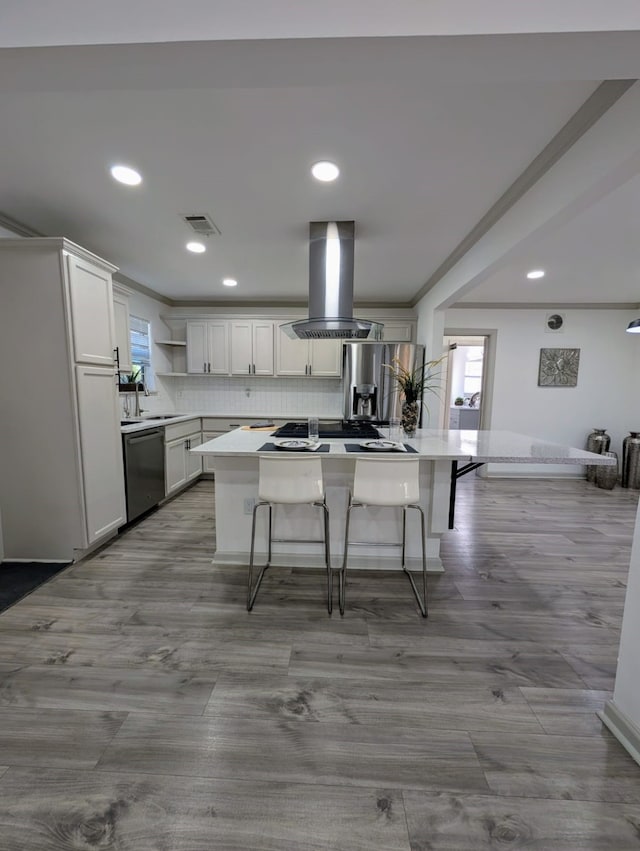 kitchen featuring a center island, stainless steel appliances, island range hood, a breakfast bar, and white cabinets