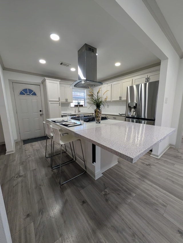 kitchen featuring a kitchen bar, stainless steel fridge, island range hood, white cabinets, and a kitchen island