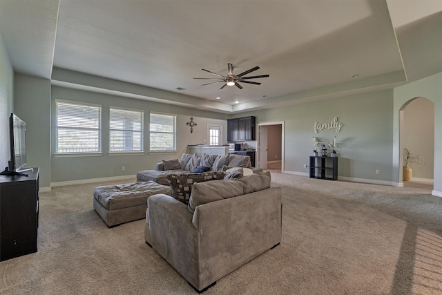 carpeted living room featuring a raised ceiling and ceiling fan