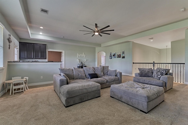 carpeted living room with ceiling fan and a tray ceiling