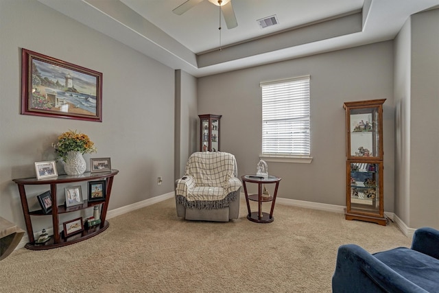 sitting room featuring a tray ceiling, ceiling fan, and light colored carpet