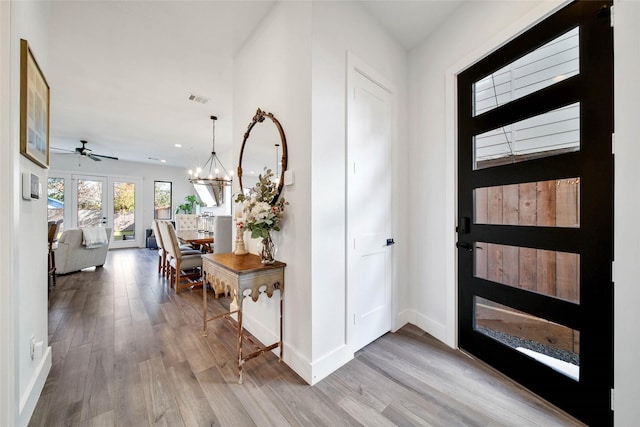 foyer entrance with french doors, wood-type flooring, and ceiling fan with notable chandelier