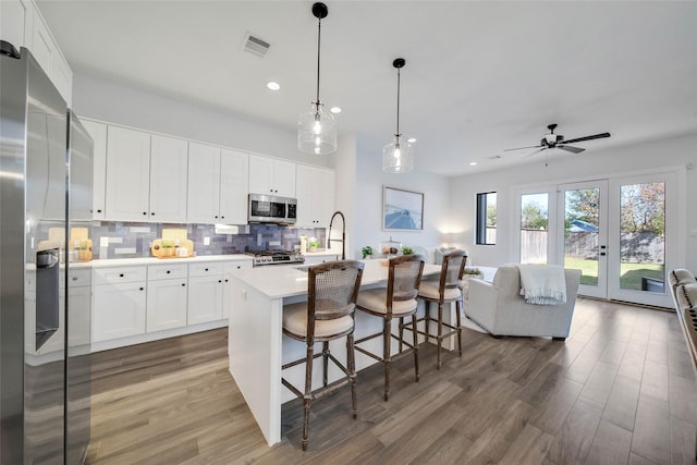 kitchen with appliances with stainless steel finishes, french doors, tasteful backsplash, a center island with sink, and white cabinets