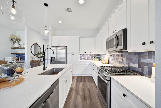 kitchen featuring backsplash, stainless steel appliances, sink, white cabinetry, and hanging light fixtures