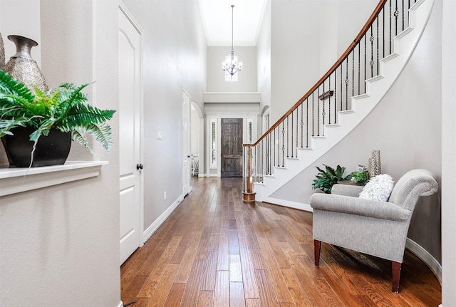 foyer entrance featuring a towering ceiling, an inviting chandelier, ornamental molding, and hardwood / wood-style floors