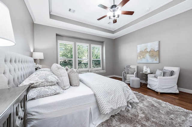 bedroom with ceiling fan, dark hardwood / wood-style flooring, ornamental molding, and a tray ceiling