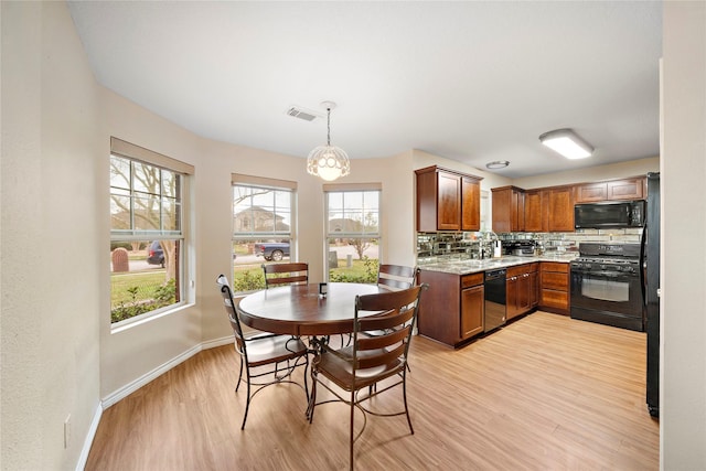 kitchen featuring black appliances, hanging light fixtures, light wood-type flooring, an inviting chandelier, and backsplash