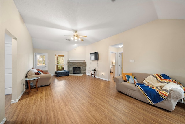 living room featuring lofted ceiling, a fireplace, ceiling fan, and light hardwood / wood-style floors