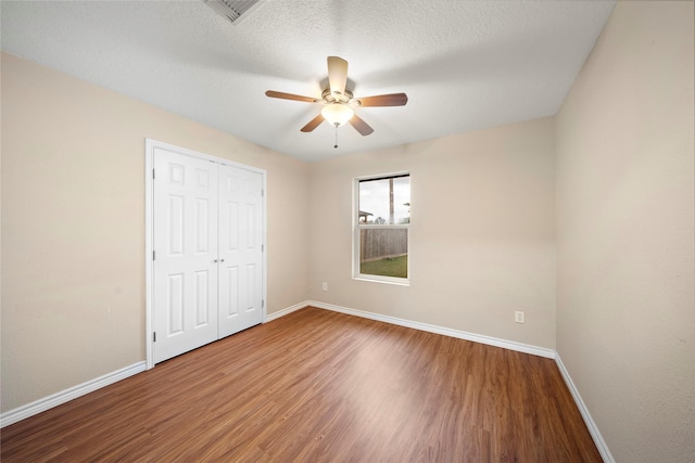 unfurnished bedroom with ceiling fan, a closet, a textured ceiling, and wood-type flooring