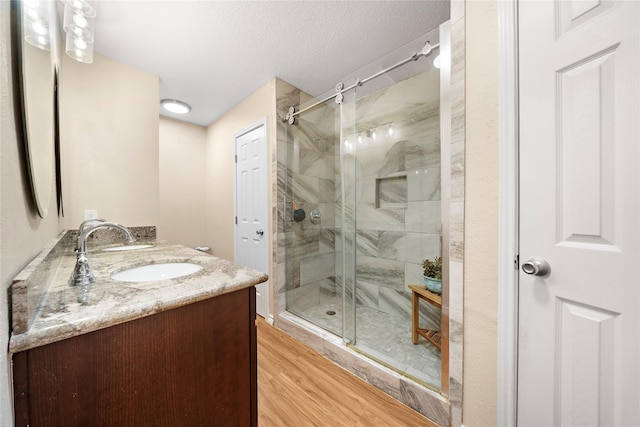 bathroom featuring vanity, wood-type flooring, an enclosed shower, and a textured ceiling