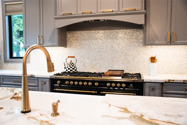 kitchen with light stone countertops, backsplash, range with two ovens, and gray cabinetry