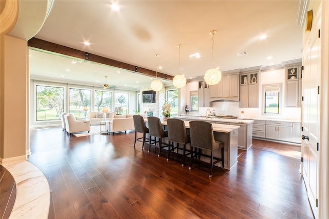 kitchen with a large island with sink, ceiling fan, dark hardwood / wood-style floors, decorative light fixtures, and beam ceiling