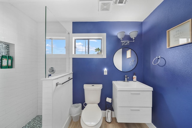 bathroom featuring tiled shower, vanity, hardwood / wood-style flooring, and toilet