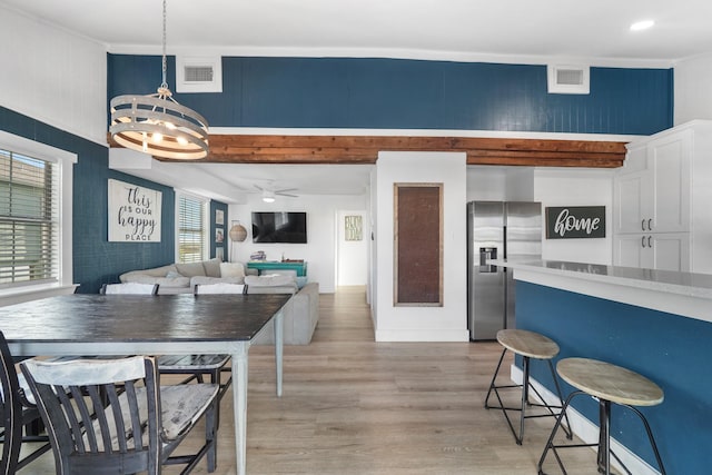 kitchen featuring pendant lighting, ceiling fan with notable chandelier, stainless steel refrigerator with ice dispenser, light hardwood / wood-style floors, and white cabinetry