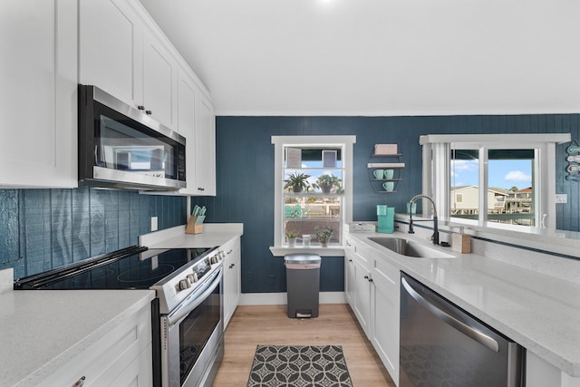 kitchen with sink, light hardwood / wood-style flooring, light stone counters, white cabinetry, and stainless steel appliances