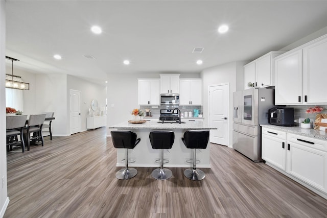 kitchen featuring stainless steel appliances, a kitchen island with sink, white cabinets, and decorative backsplash