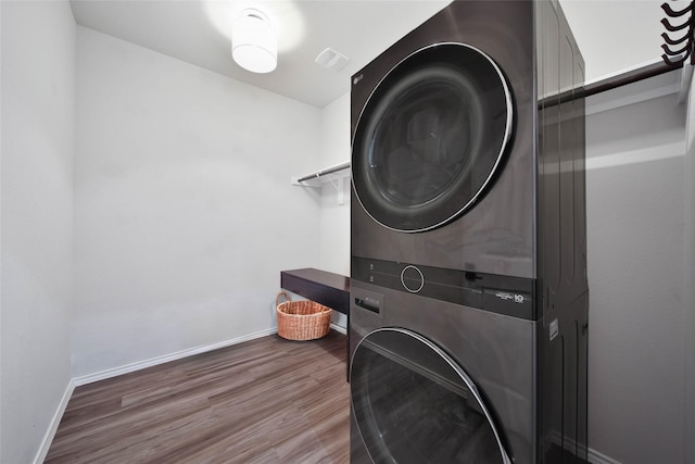 clothes washing area with stacked washer / drying machine and dark wood-type flooring