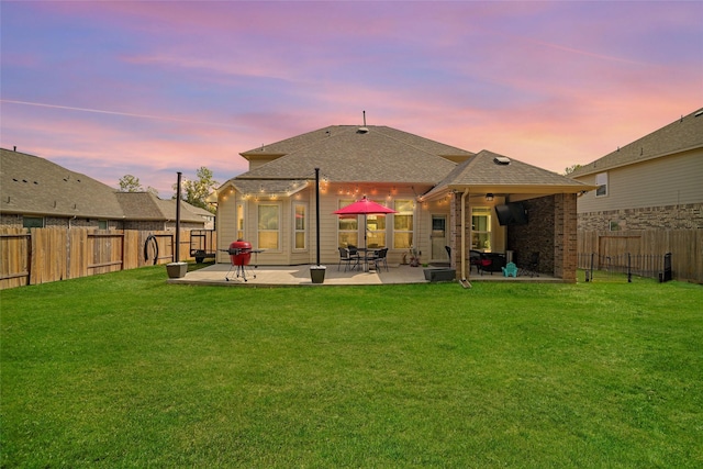 back house at dusk with a patio area and a yard