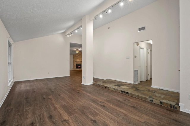 unfurnished living room with lofted ceiling, dark wood-type flooring, track lighting, a textured ceiling, and a large fireplace