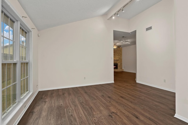 spare room featuring ceiling fan, a large fireplace, rail lighting, dark wood-type flooring, and vaulted ceiling