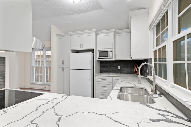 kitchen with a textured ceiling, sink, white cabinets, white fridge, and stainless steel microwave