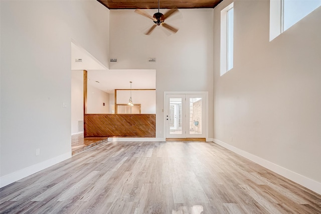 unfurnished living room featuring ceiling fan, wooden ceiling, a high ceiling, and light hardwood / wood-style flooring