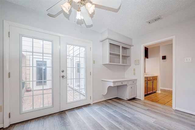 doorway with ceiling fan, light hardwood / wood-style floors, and a textured ceiling