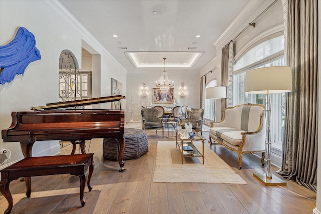 sitting room with a raised ceiling, light wood-type flooring, crown molding, and an inviting chandelier