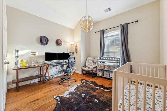 bedroom featuring vaulted ceiling, a crib, and hardwood / wood-style flooring