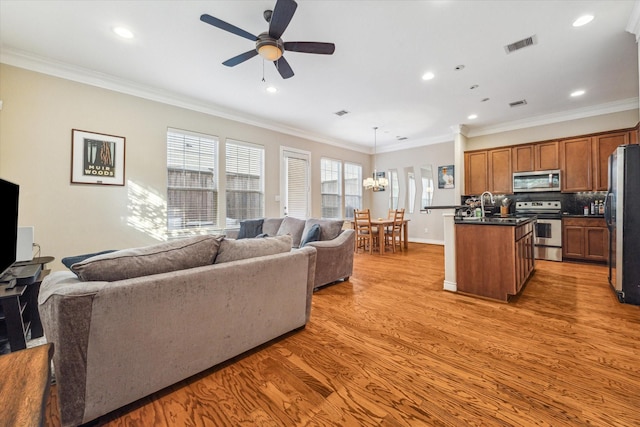 living room featuring ceiling fan with notable chandelier, light hardwood / wood-style flooring, ornamental molding, and sink