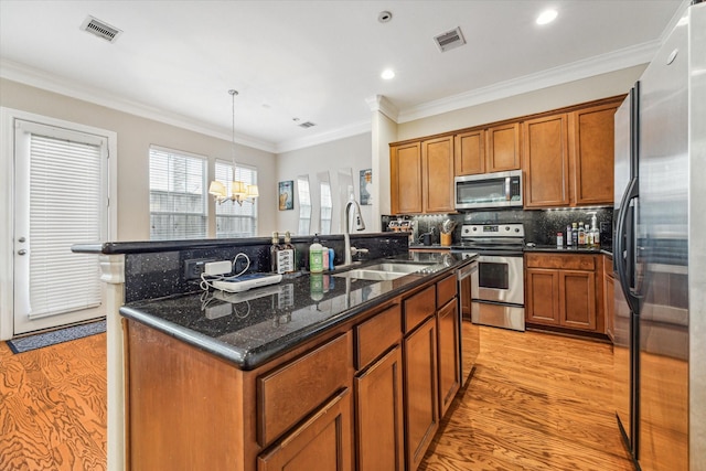 kitchen with appliances with stainless steel finishes, sink, dark stone countertops, light hardwood / wood-style floors, and hanging light fixtures