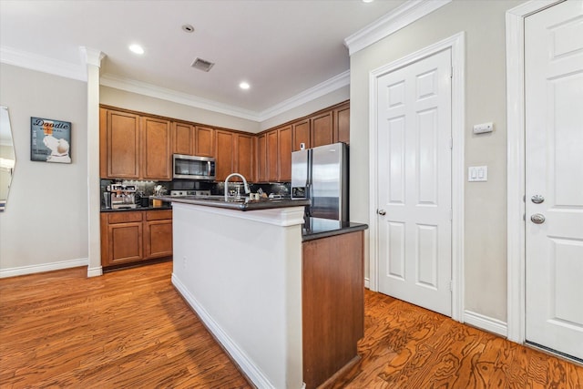 kitchen featuring decorative backsplash, stainless steel appliances, crown molding, wood-type flooring, and an island with sink