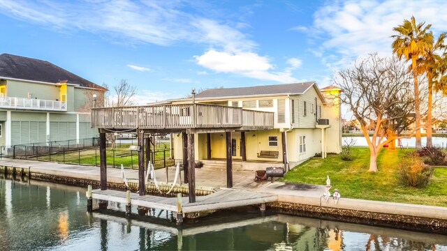 back of house featuring a lawn, a deck with water view, and a patio