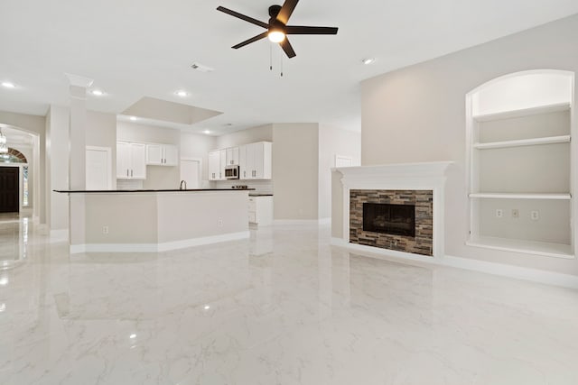 unfurnished living room with ceiling fan and a stone fireplace