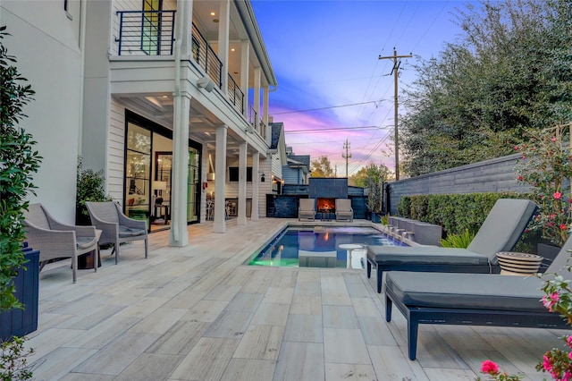 pool at dusk with an outdoor fireplace and a patio area