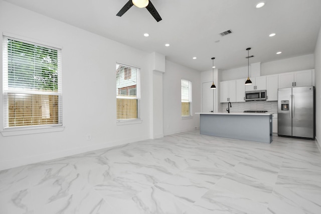 kitchen with decorative light fixtures, a center island with sink, white cabinetry, appliances with stainless steel finishes, and ceiling fan