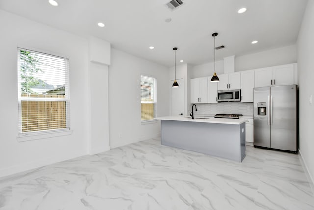 kitchen with appliances with stainless steel finishes, an island with sink, white cabinets, decorative light fixtures, and sink