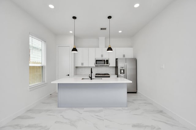 kitchen featuring stainless steel appliances, an island with sink, white cabinets, decorative light fixtures, and tasteful backsplash