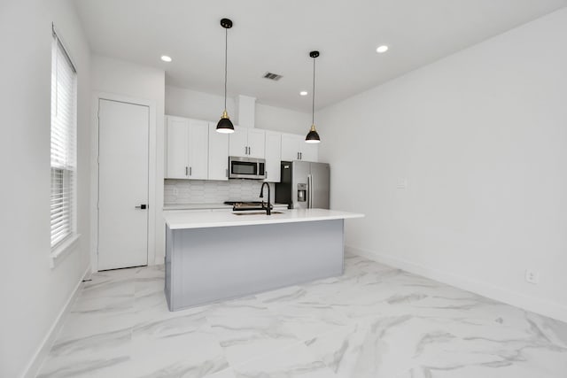 kitchen with decorative light fixtures, stainless steel appliances, a center island with sink, white cabinetry, and sink