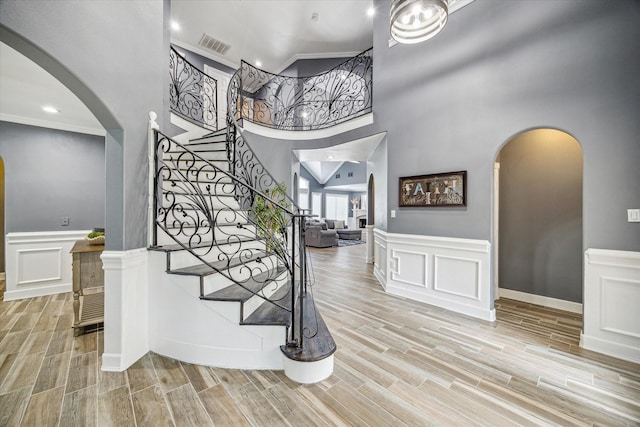 foyer entrance with a towering ceiling, light wood-type flooring, and ornamental molding