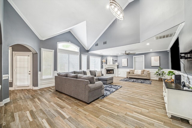 living room with light hardwood / wood-style floors, ceiling fan, ornamental molding, and high vaulted ceiling